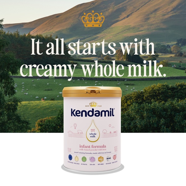A high-contrast 1:1 image featuring an infant formula tin placed in front of a lush, rolling green countryside landscape.